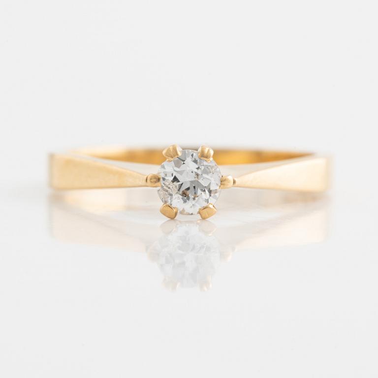 An 18K gold ring set with a round brilliant-cut diamond.