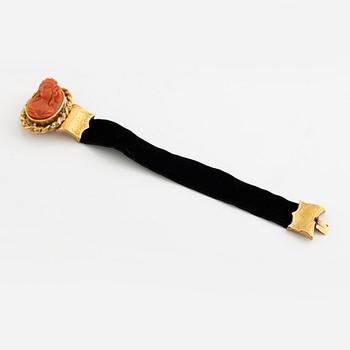 An 18K gold and coral cameo braclet with a black band.