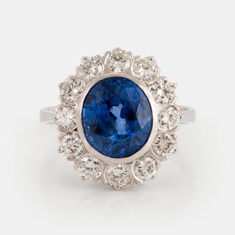 An 18K white gold ring set with a faceted sapphire and round brilliant-cut diamonds.