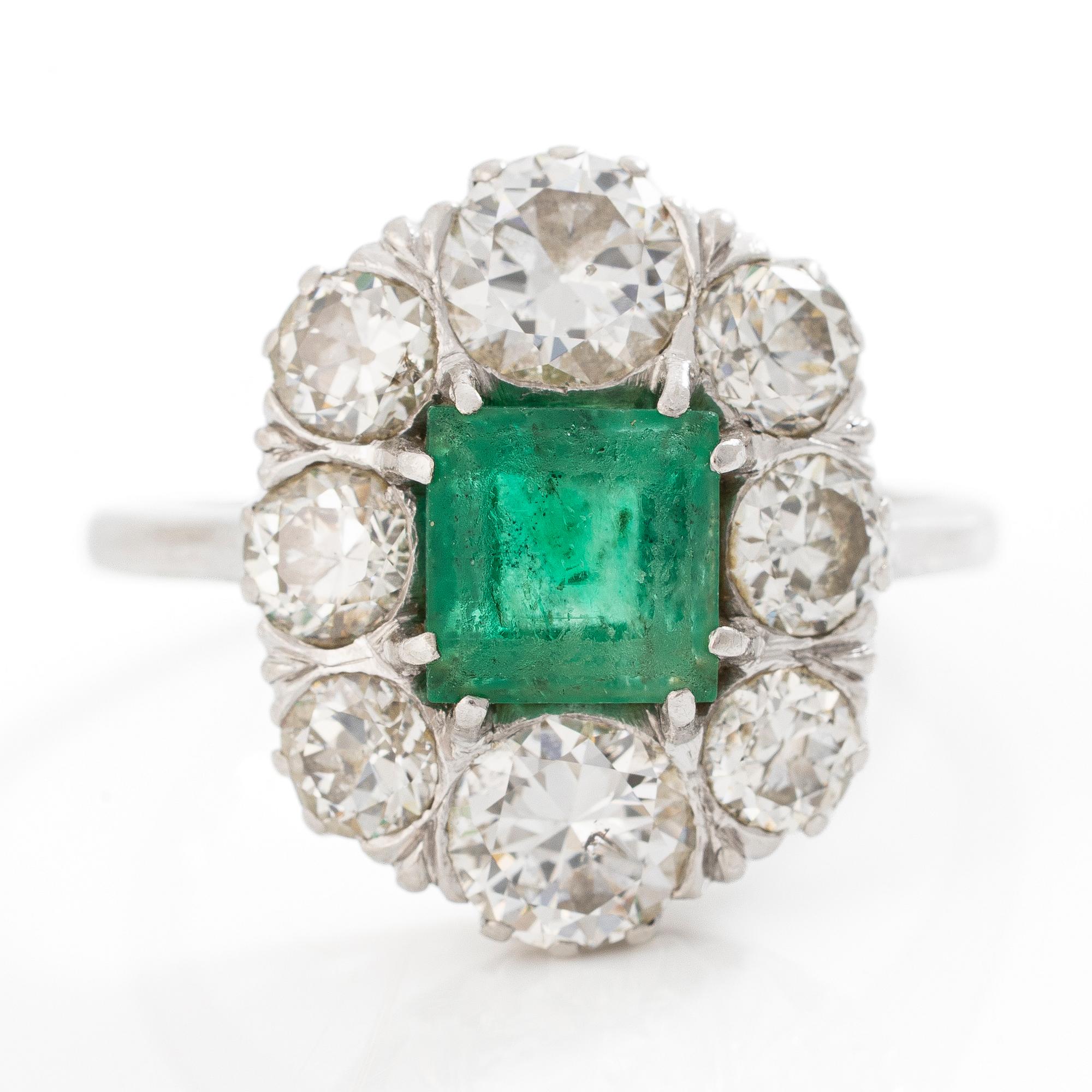 18K white gold ring set with a faceted emerald and round brilliant-cut diamonds.