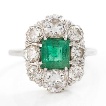 18K white gold ring set with a faceted emerald and round brilliant-cut diamonds.