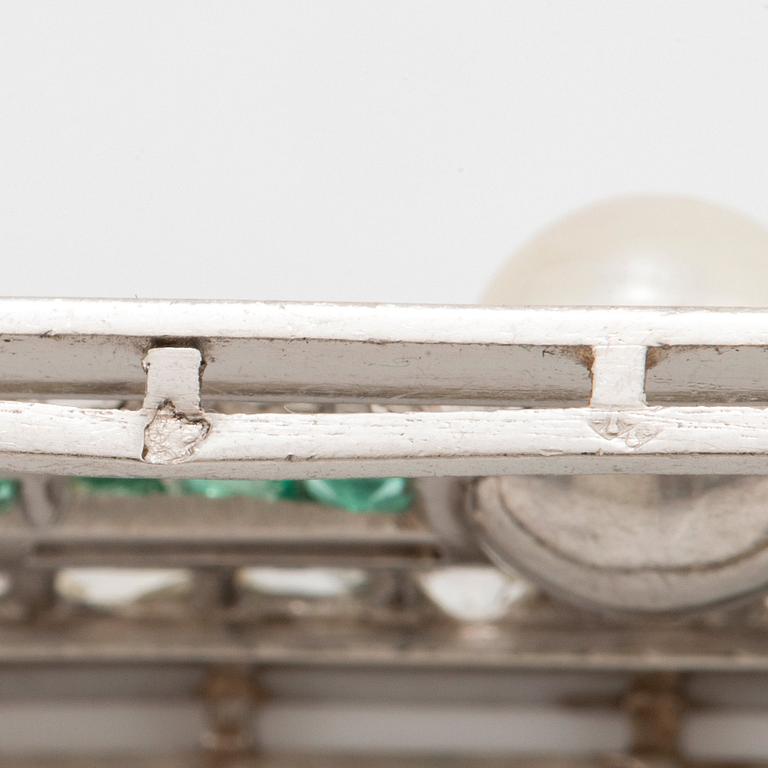 A platinum brooch set with old- and rose-cut diamonds, faceted emeralds and a pearl.