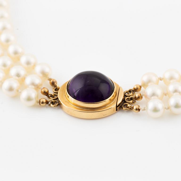 A three strand cultured pearls neckace clasp 18K gold with a purple stone, likely amethyst.