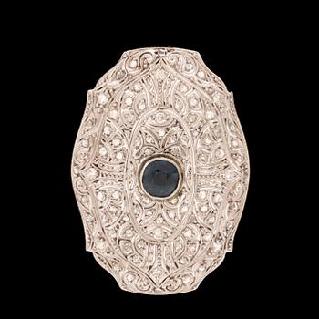 An 18K white gold brooch set with a facet-cut sapphire possibly synthetic, as well as brilliant and rose-cut diamonds.