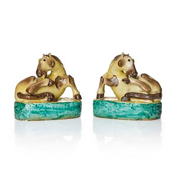 A pair of green, yellow and aubergine glazed biscuit figures of recumbent horses, Qing dynasty.