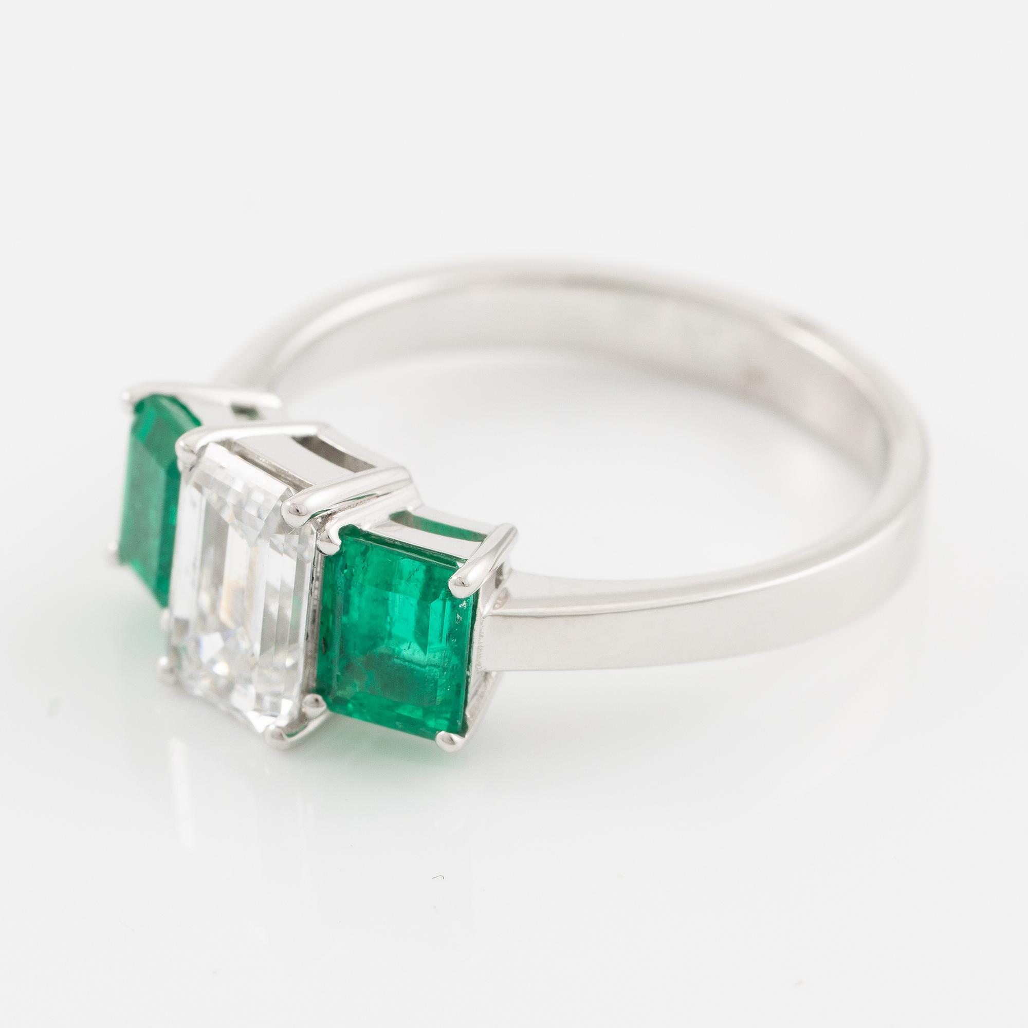 An 18K white gold ring set with an emerald-cut diamond and two step-cut emeralds.
