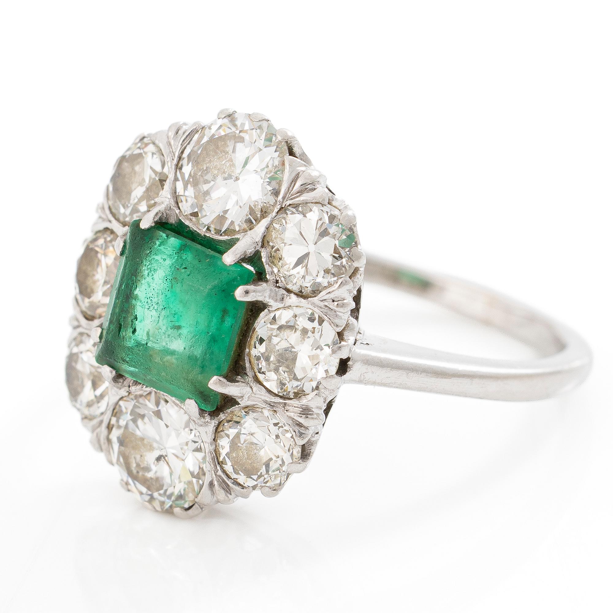 18K white gold ring set with a faceted emerald and round brilliant-cut diamonds.
