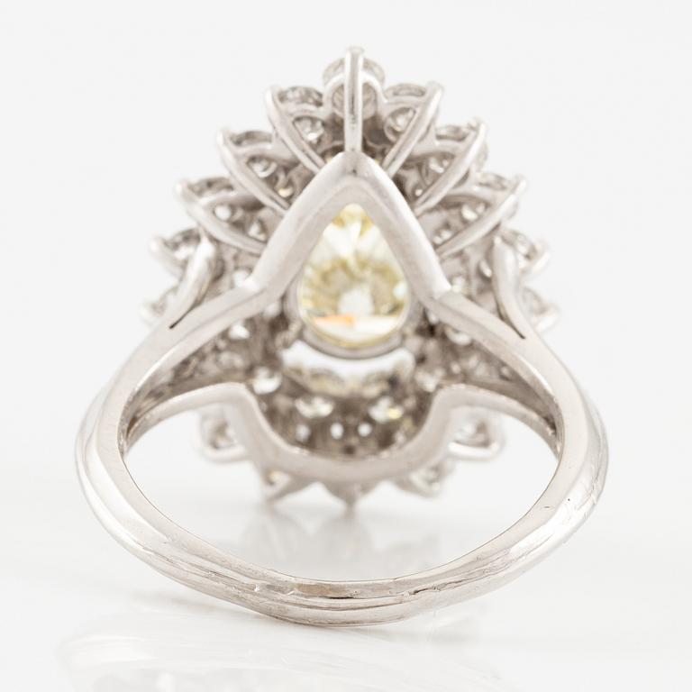 A platinum ring set with a pear-shaped yellow diamond and round brilliant-cut diamonds.