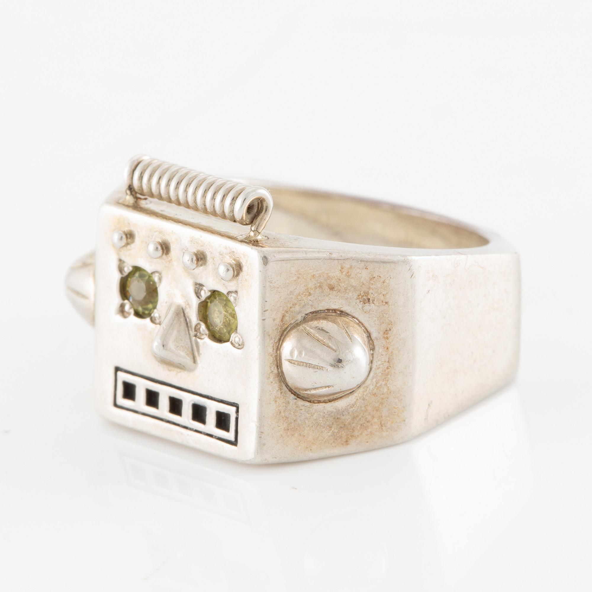 Maria Nilsdotter ring i form av ett robothuvud, sterlingsilver och gröna ögon.