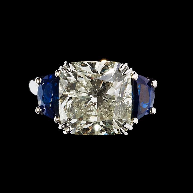 RING, cushion cut diamant, 6.52 ct med blå safirer fattade på vardera sida.