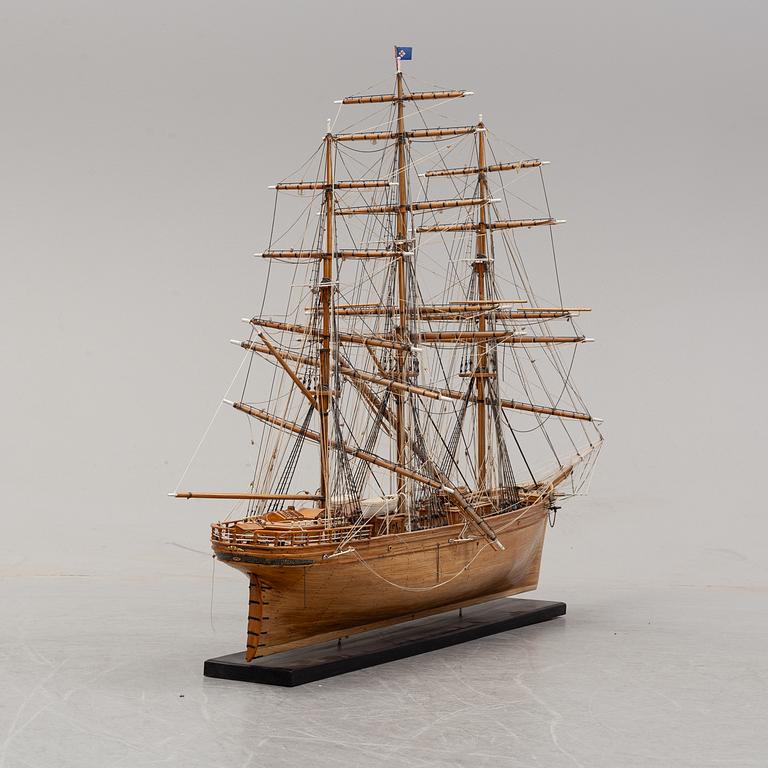 A wooden scale model of Cutty Sark on a painted wooden stand.