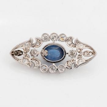 A platinum brooch set with a cabochon-cut sapphire and a cabochon-cut emerald.