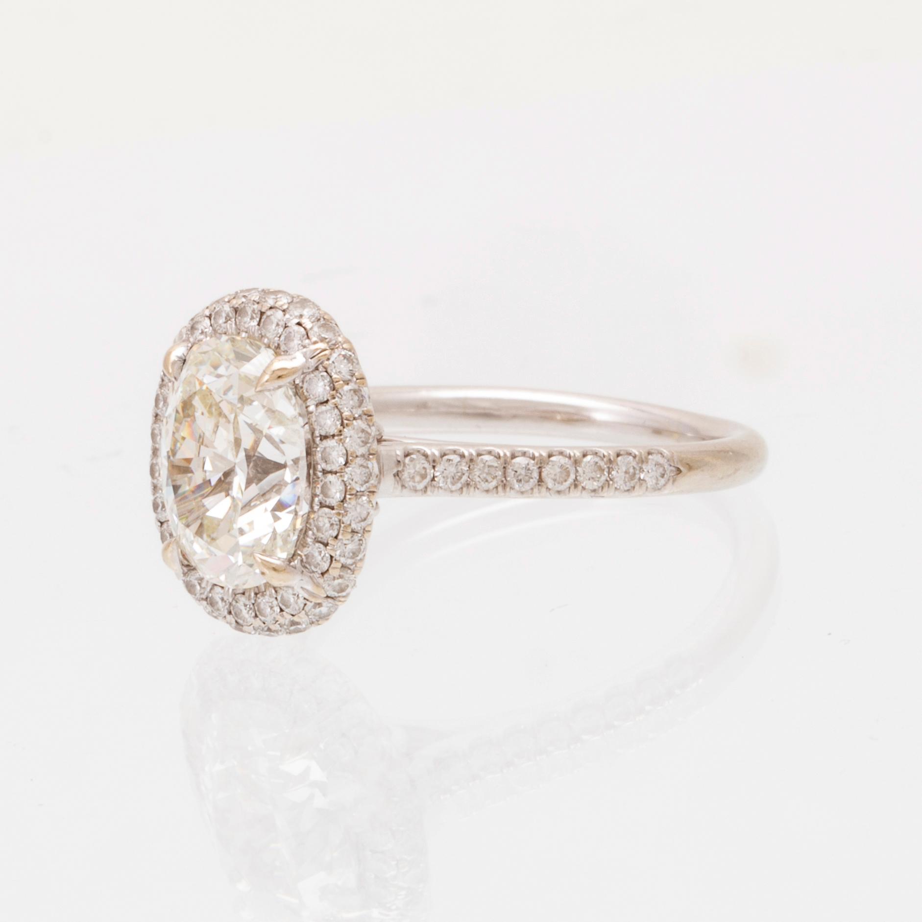 An 18K white gold ring by James Allen, set with an oval brilliant cut diamond in a halo of round brilliant cut diamonds.