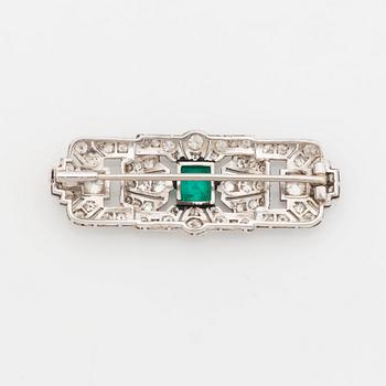 A platinum brooch set with a step-cut emerald and old- and eight-cut diamonds.