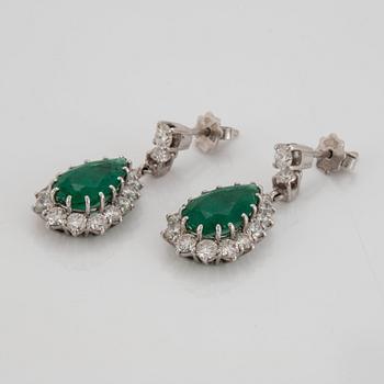 Ett par örhängen med droppformade fasettslipade smaragder samt runda briljantslipade diamanter.