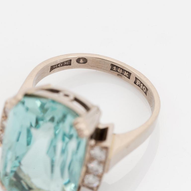 An 18K white gold ring set with a faceted aquamarine and round brilliant-cut diamonds.