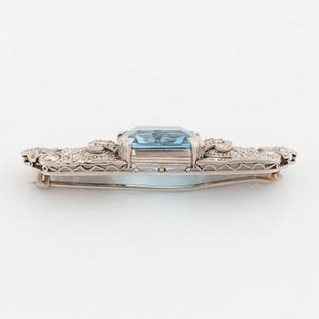 An 18K white gold brooch set with a faceted aquamarine and round brilliant- and rose-cut diamonds.