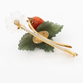 A flower brooch 18K gold with coral, rock crystal, a green stone likely nephrite, and a round brilliant-cut diamond.