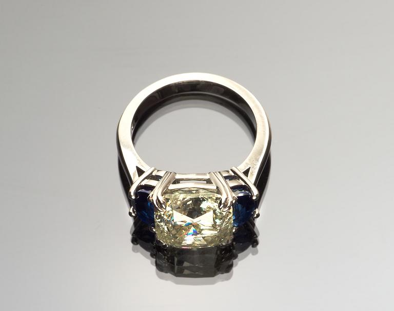 RING, cushion cut diamant, 6.52 ct med blå safirer fattade på vardera sida.