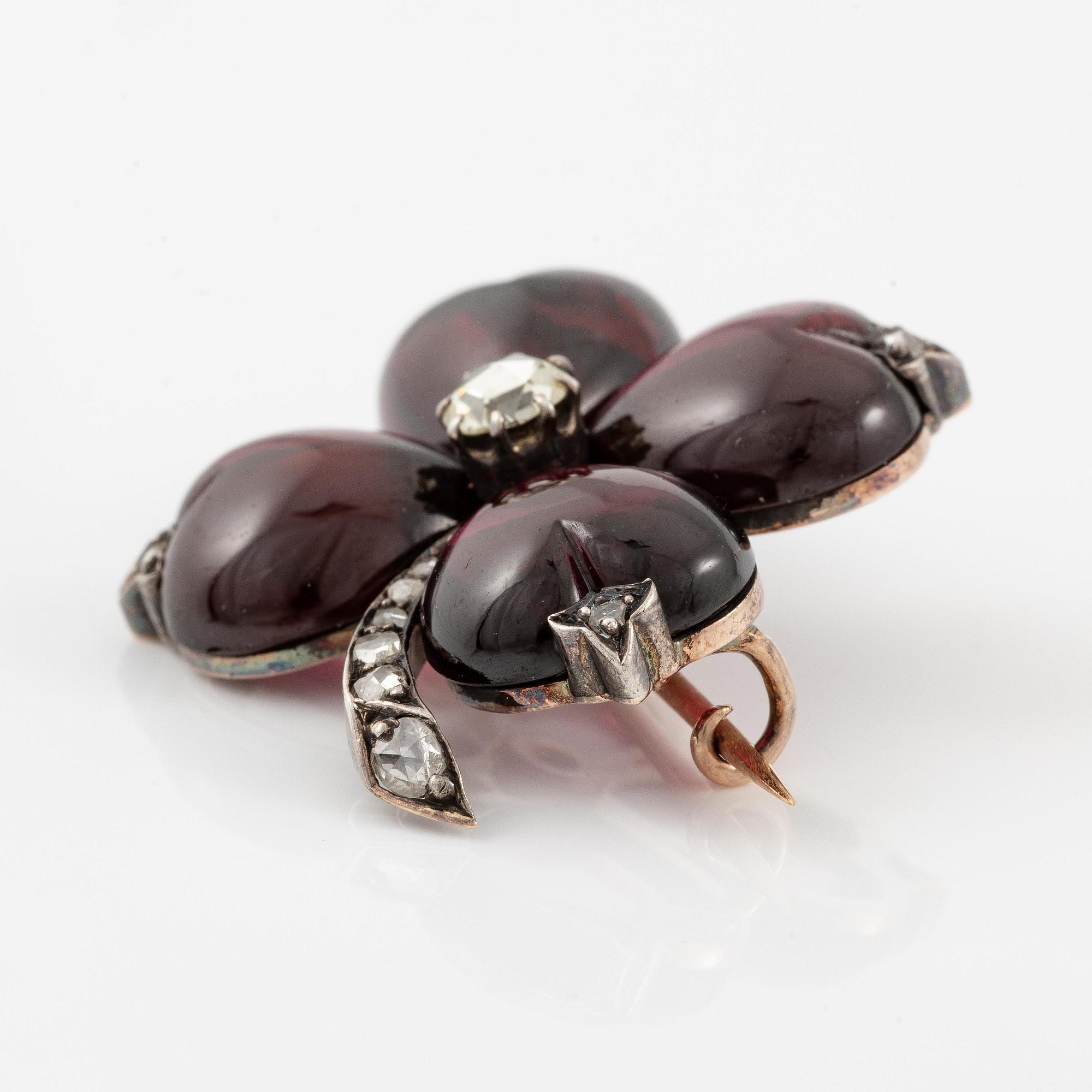 A brooch in the shape of a four-leaf clover, gold and silver with garnets and rose-cut diamonds.