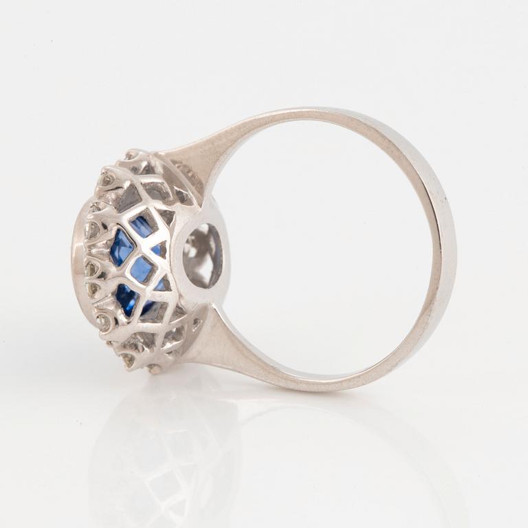 An 18K white gold ring set with a faceted sapphire and round brilliant-cut diamonds.