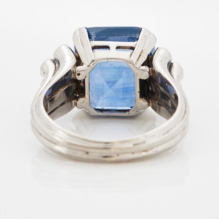 An 18K white gold ring set with a faceted sapphire and round brilliant-cut diamonds.