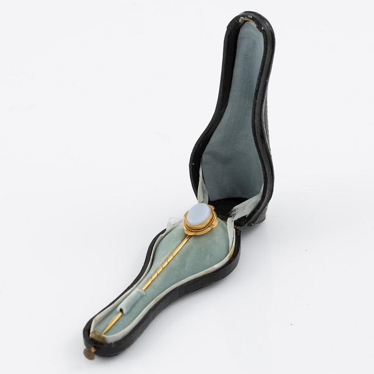 Brooch pin of low-grade gold with a white-blue stone.