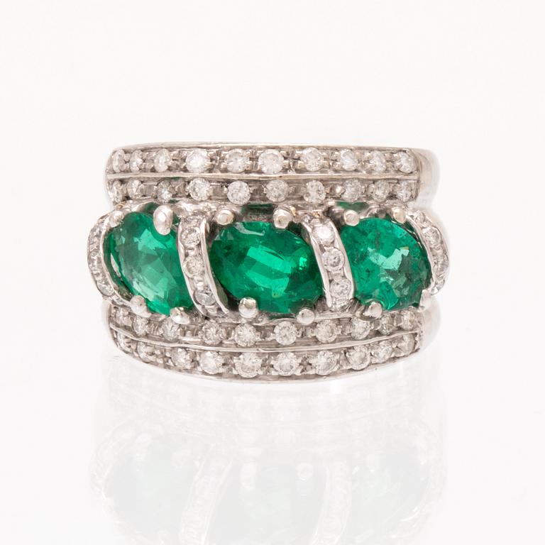 An 18K white gold ring set with oval cut emeralds and round brilliant cut diamonds.