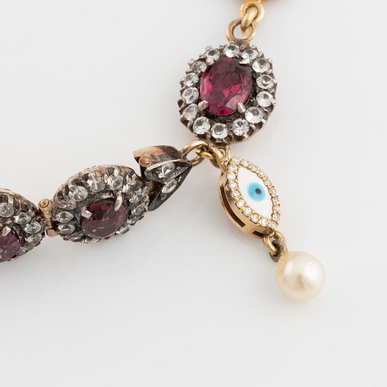 Bracelet with garnets and white stones, two charms, one eye enamel with brilliant cut diamonds, possibly oriental pearl.