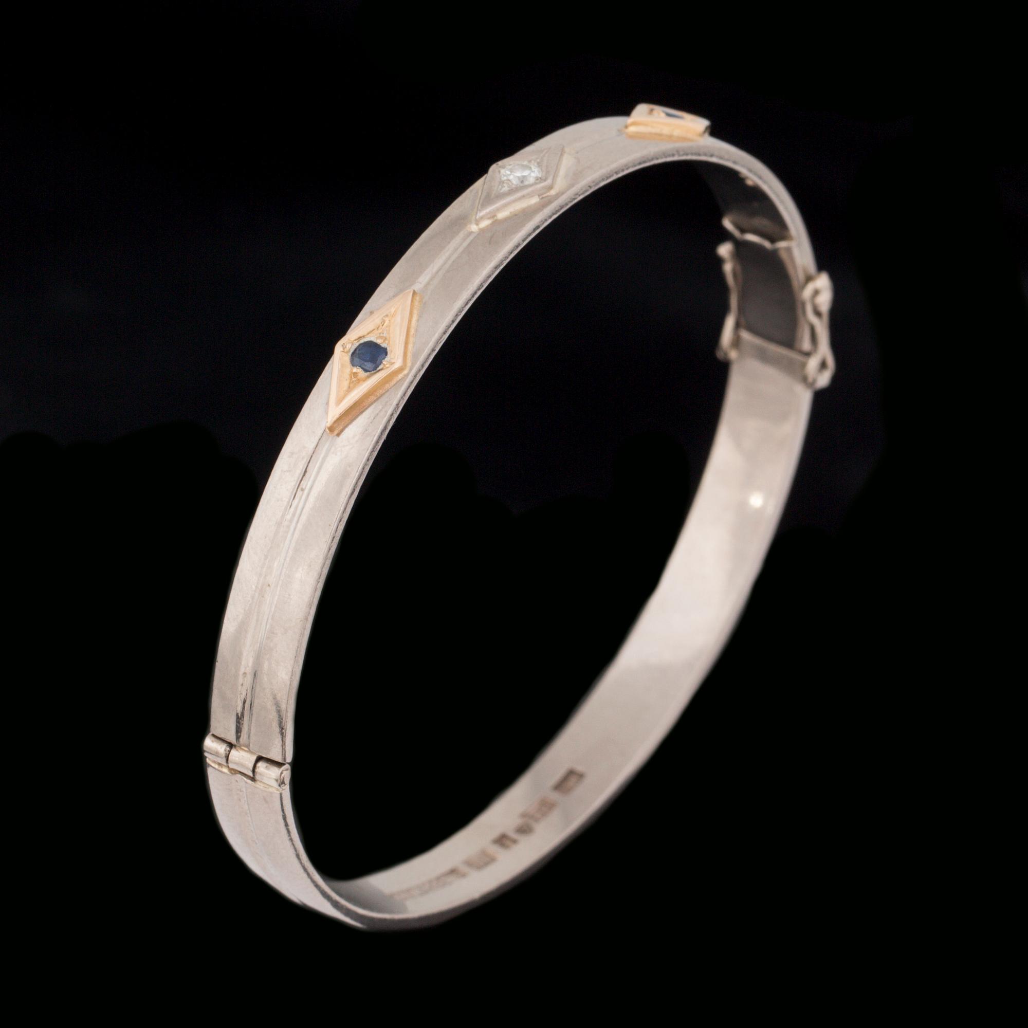 ARMRING, 18 k vitguld med briljantslipad diamant ca 0.05 ct samt 2 fasettslipade safirer. Vikt ca 33 g.