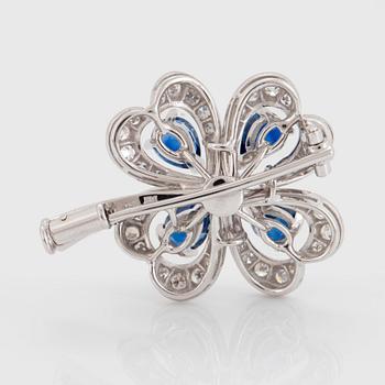 A Meister brooch in 18K white gold set with faceted sapphires, a round brilliant-cut diamond.