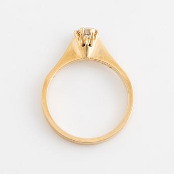 An 18K gold ring set with a round brilliant-cut diamond.