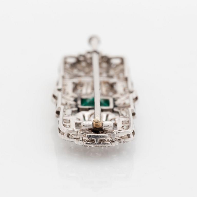 A platinum brooch set with a step-cut emerald and old- and eight-cut diamonds.