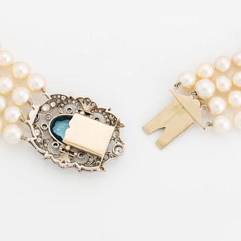 A four strand cultured pearl necklace with a clasp in 14K gold set with a faceted aquamarine.
