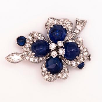 A white gold brooch with cabochon-cut sapphires, brilliant, single, marquise and baguette cut diamonds.