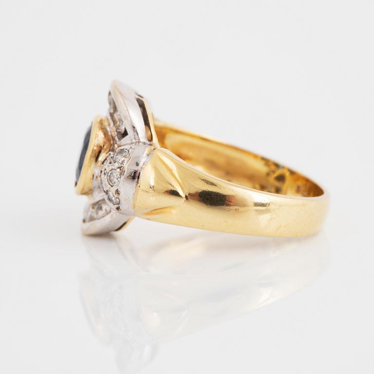 An 18K gold ring set with a synthetic sapphire and round brilliant-cut diamonds.