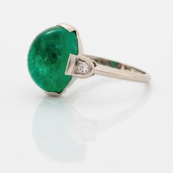 A platinum ring set with a cabochon-cut emerald and round brilliant-cut diamonds.