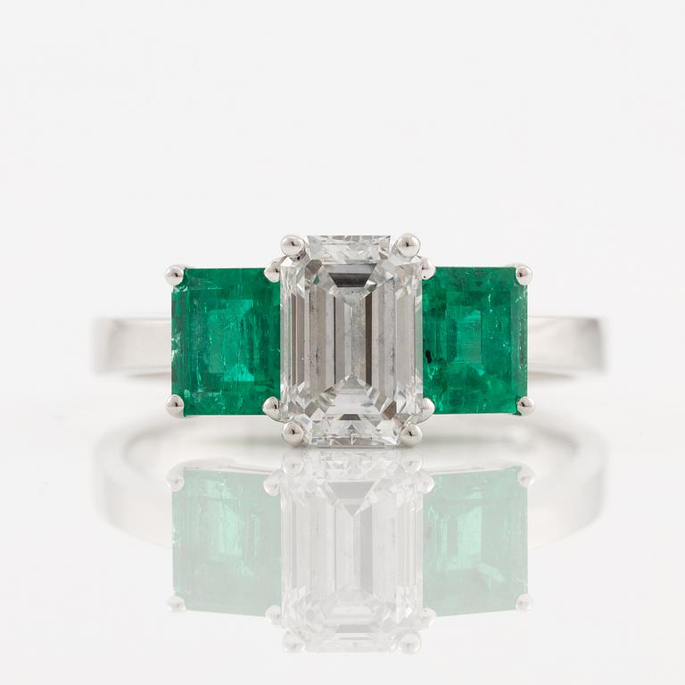 An 18K white gold ring set with an emerald-cut diamond and two step-cut emeralds.