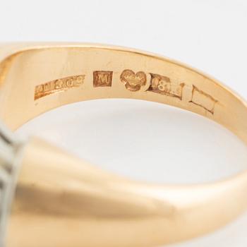 An 18K gold ring set with a step-cut emerald and round brilliant-cut diamonds.