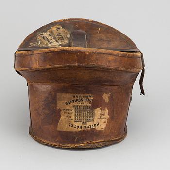 A LEATHER HAT BOX WITH A TOP HAT, 19th century latter part / turn of the century 1900.