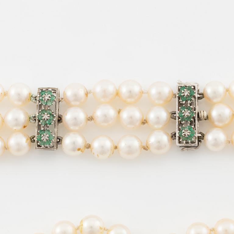 A three strand cultured pearl necklace, clasp in 18K gold with white stones and emeralds.