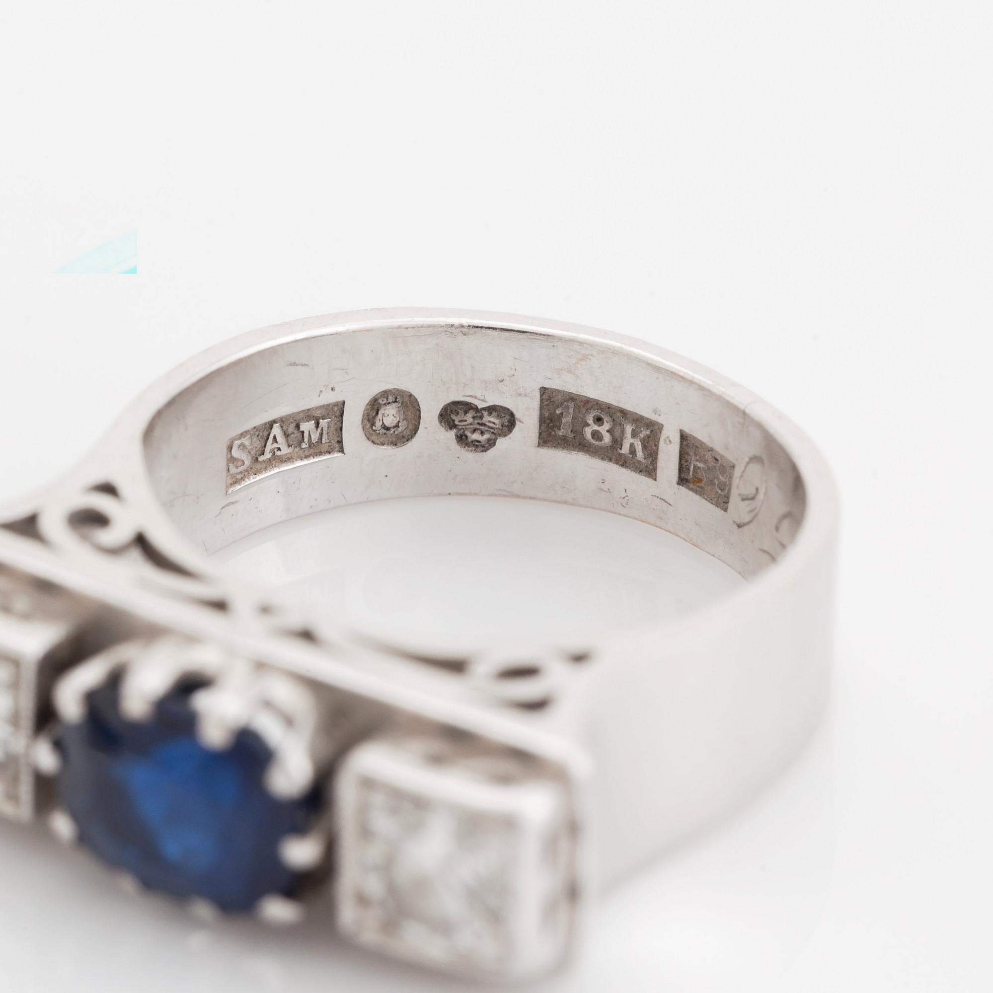 An 18K white gold ring set with a faceted sapphire, possibly synthetic, and round brilliant-cut diamonds.