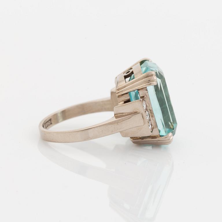 An 18K white gold ring set with a faceted aquamarine and round brilliant-cut diamonds.