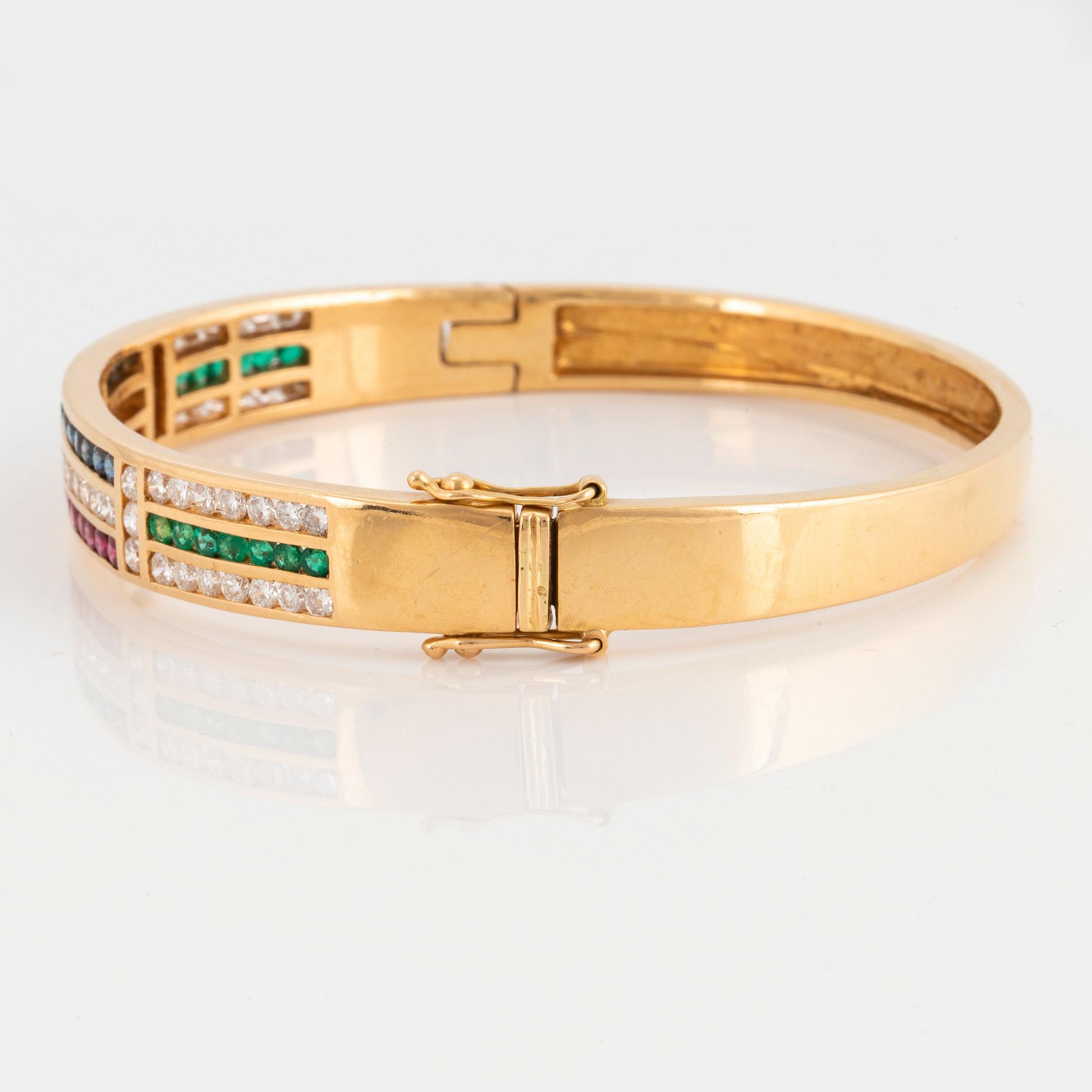 An 18K gold bangle set with round brilliant-cut diamonds, sapphires, emeralds and rubies.