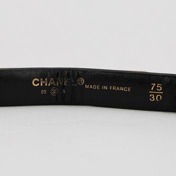 CHANEL, a skinny black leather belt with gold colored hardwear.