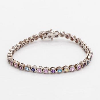 Rannekoru, 18K valkokultaa ja monivärisiä kiviä.