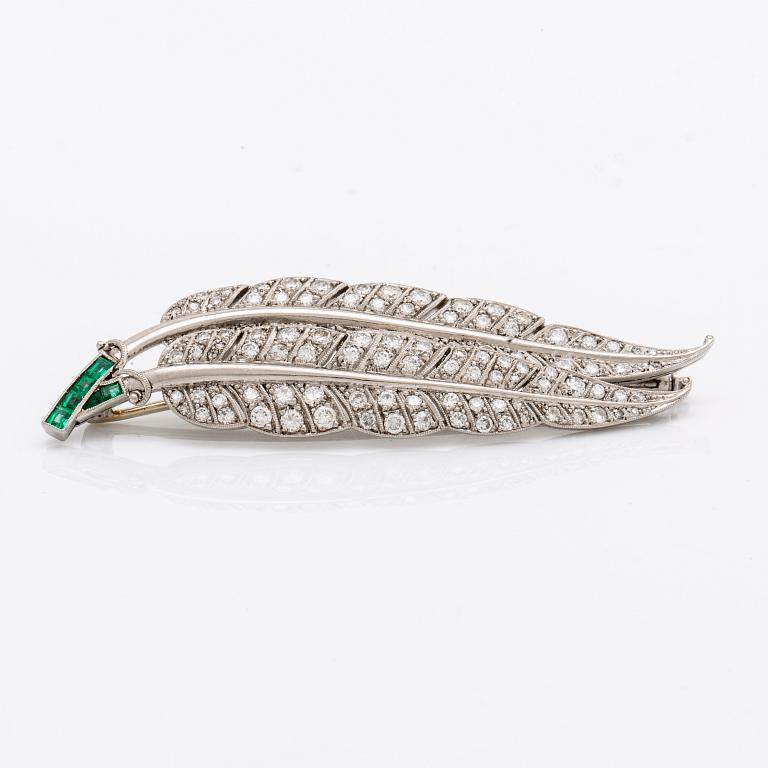 A platinum brooch set with round brilliant-cut diamonds and emeralds.