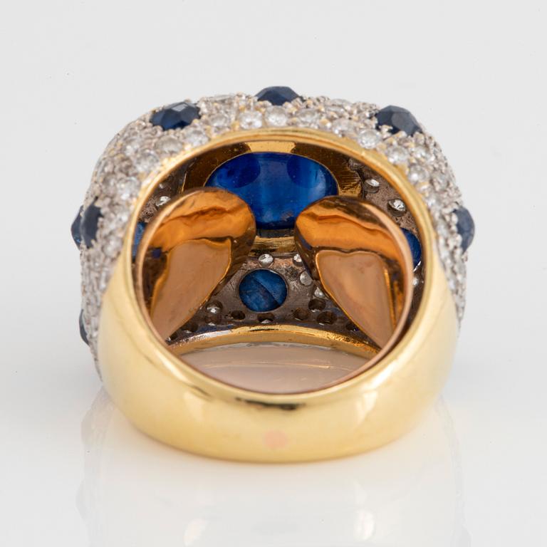 An 18K gold ring set with a cabochon-cut sapphire and round brilliant-cut diamonds and faceted sapphires.