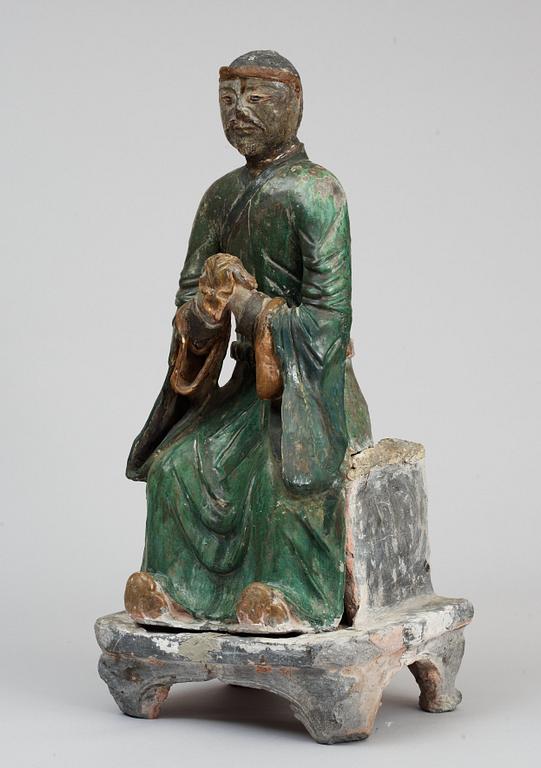 A green and yellow glazed pottery figure of a guardsman, seated on a postament, Ming dynasty.