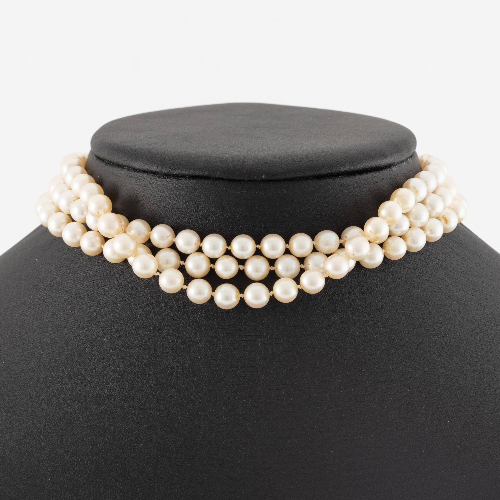 A three strand cultured pearl necklace, clasp in 18K gold with white stones and emeralds.